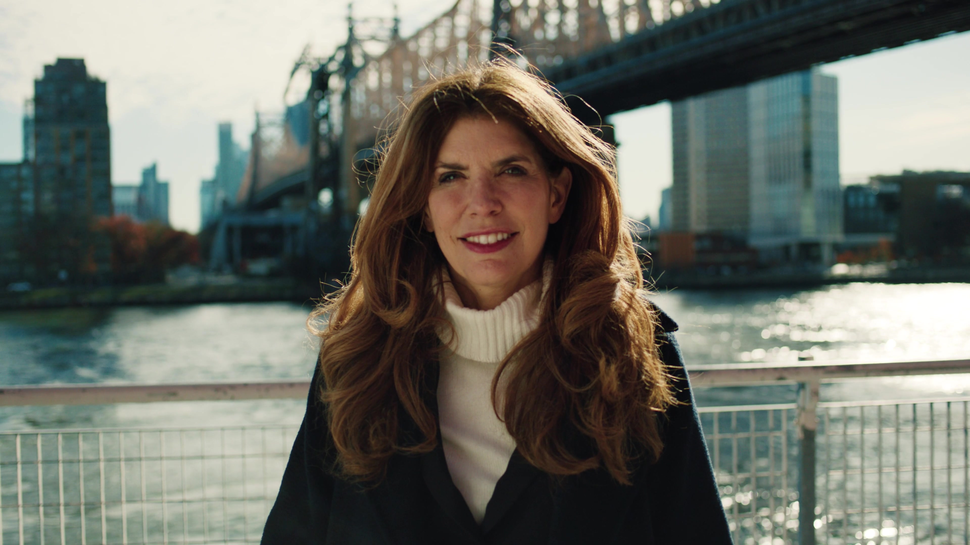 Julie Menin smiling toward the camera beside the river and bridge